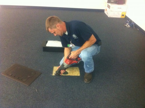 Dan House Electric technician inspecting and updating an existing floor outlet